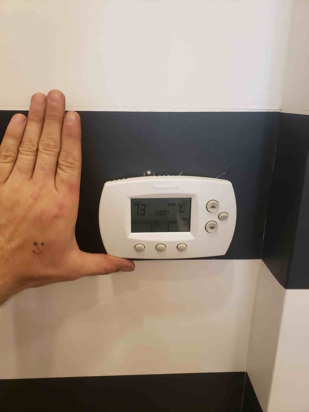 Hand next to a thermostat displaying 73°F set temperature on a striped wall.