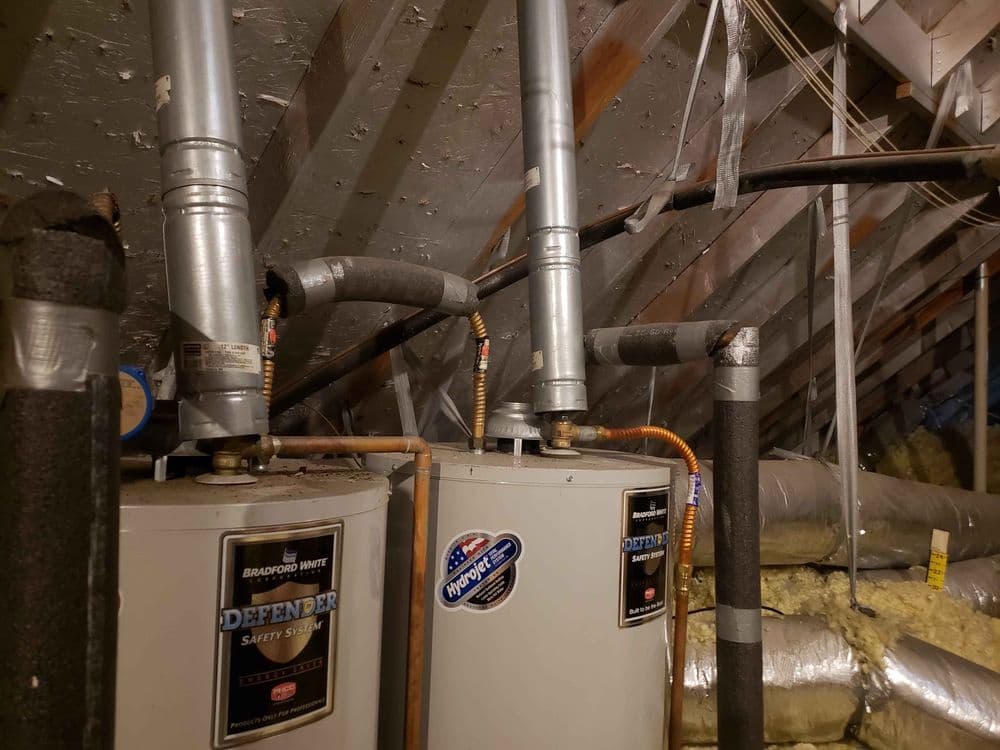 Two water heaters in an attic with ventilation pipes and insulation visible.