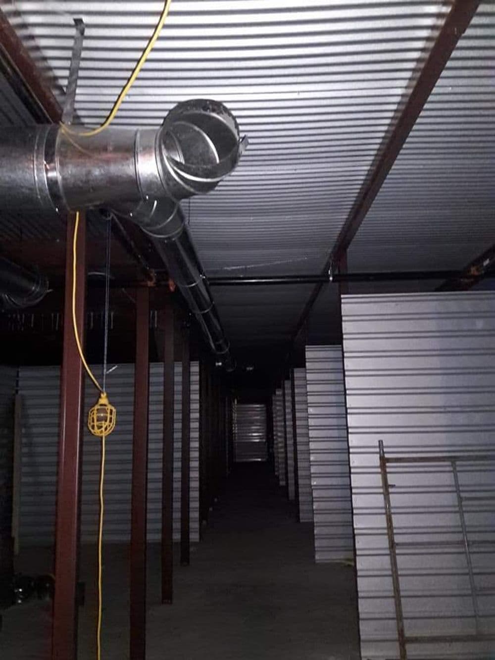 View of a dimly lit storage facility with metal walls and ductwork overhead.