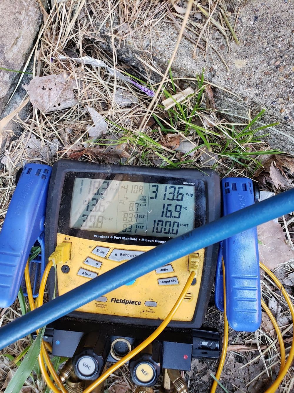 Fieldpiece digital manifold gauge displaying pressure and temperature readings in a grassy area.