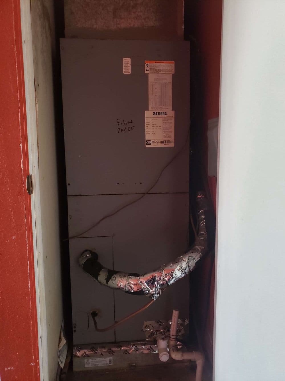 Furnace unit in a narrow hallway with metal ducting and insulation.