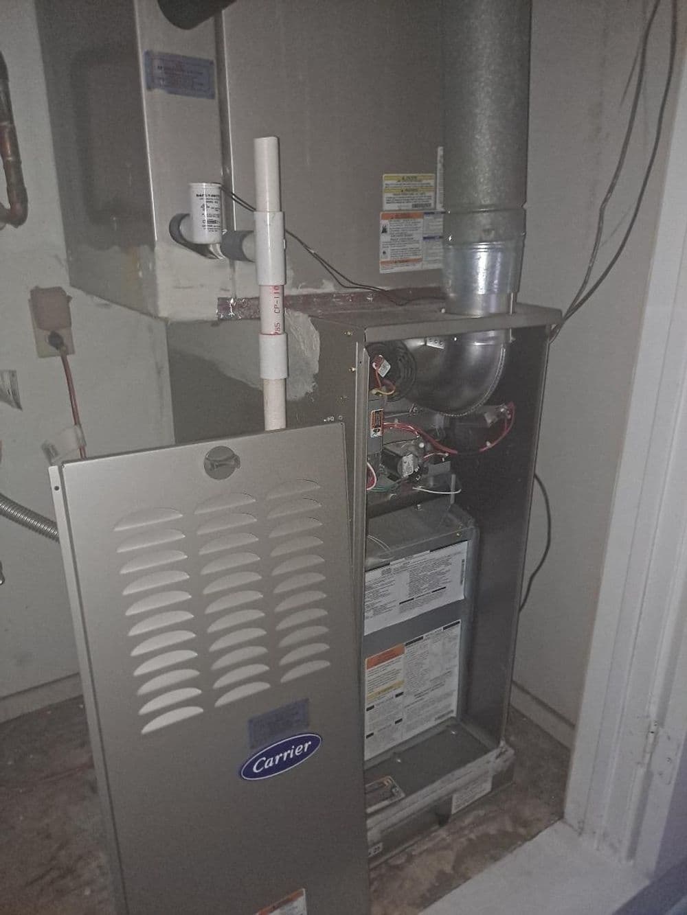 Carrier furnace with open panel, showing interior components and venting in a utility room.