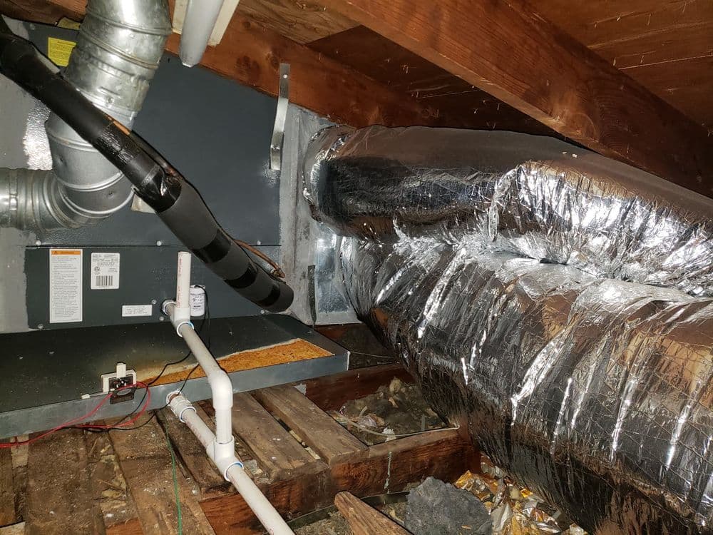 Ductwork and HVAC system in an attic with exposed plumbing and insulation details.