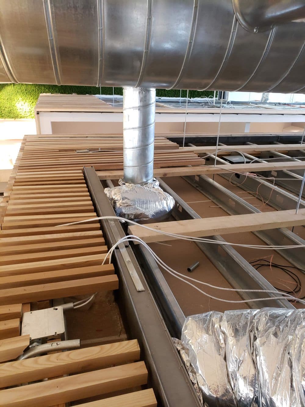 Ductwork installation on a wooden ceiling frame with insulation and electrical wires visible.