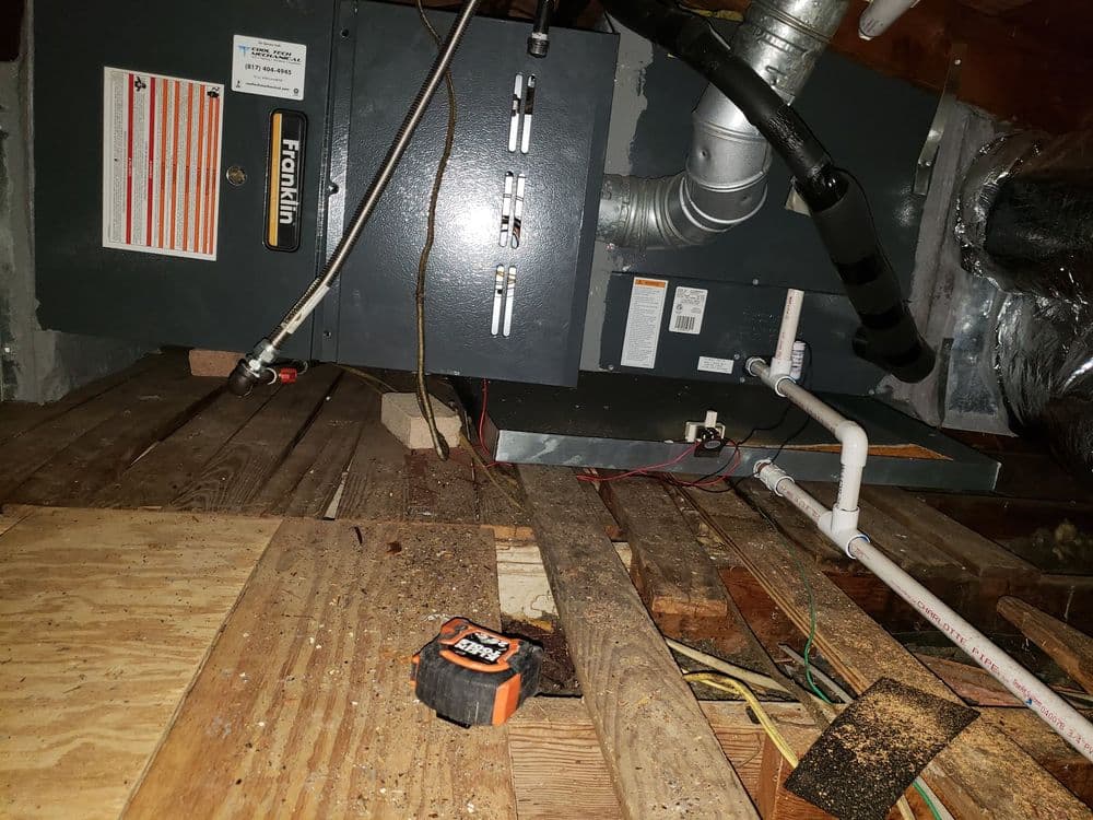 Franklin furnace in attic with wooden beams, pipes, and measuring tape on floor.