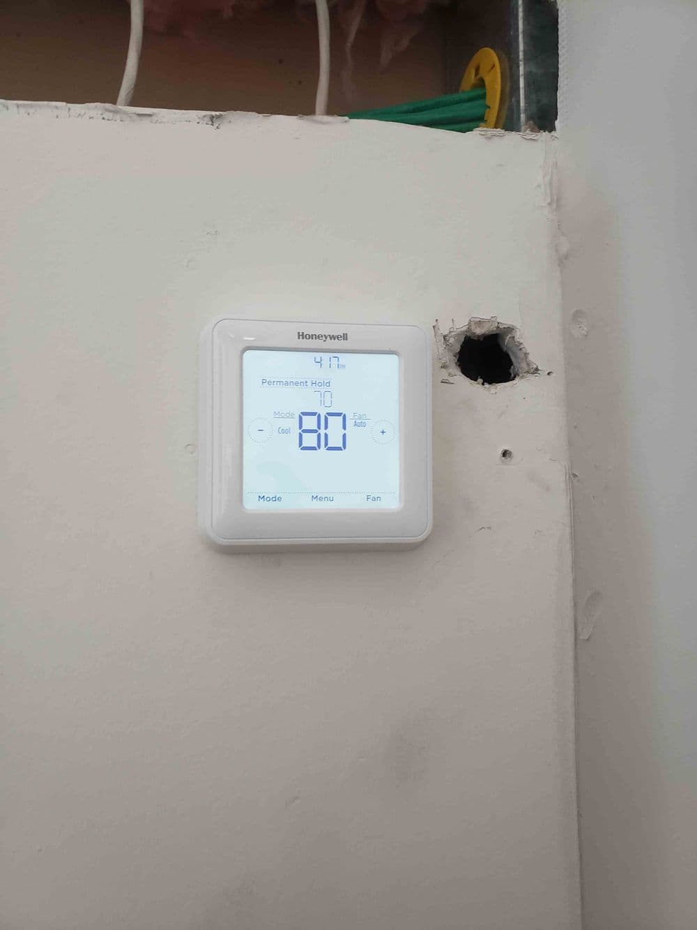 Honeywell thermostat displaying temperature settings on a wall, with installation hole nearby.