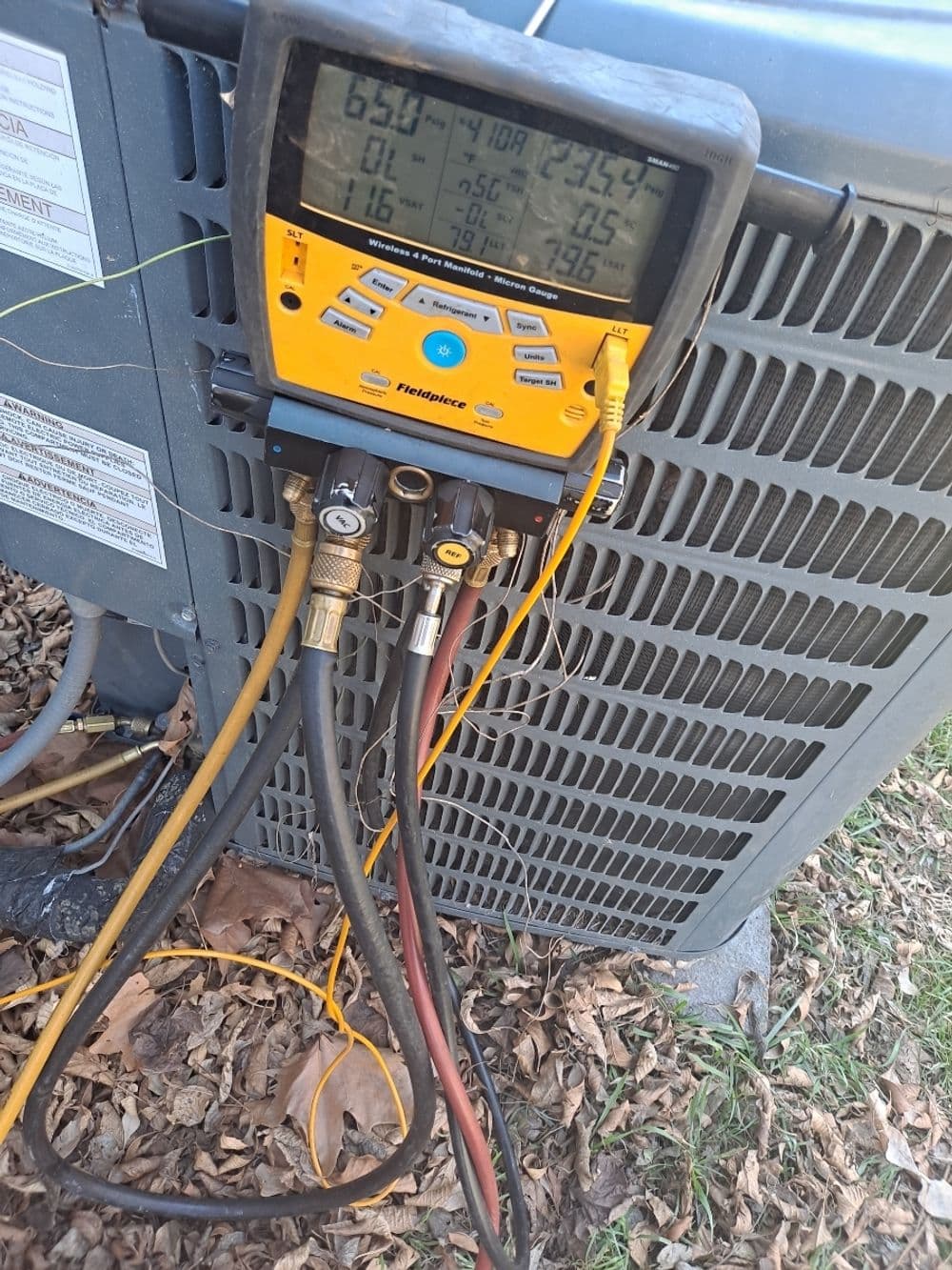 HVAC manifold gauge on air conditioning unit displaying temperature and pressure readings.