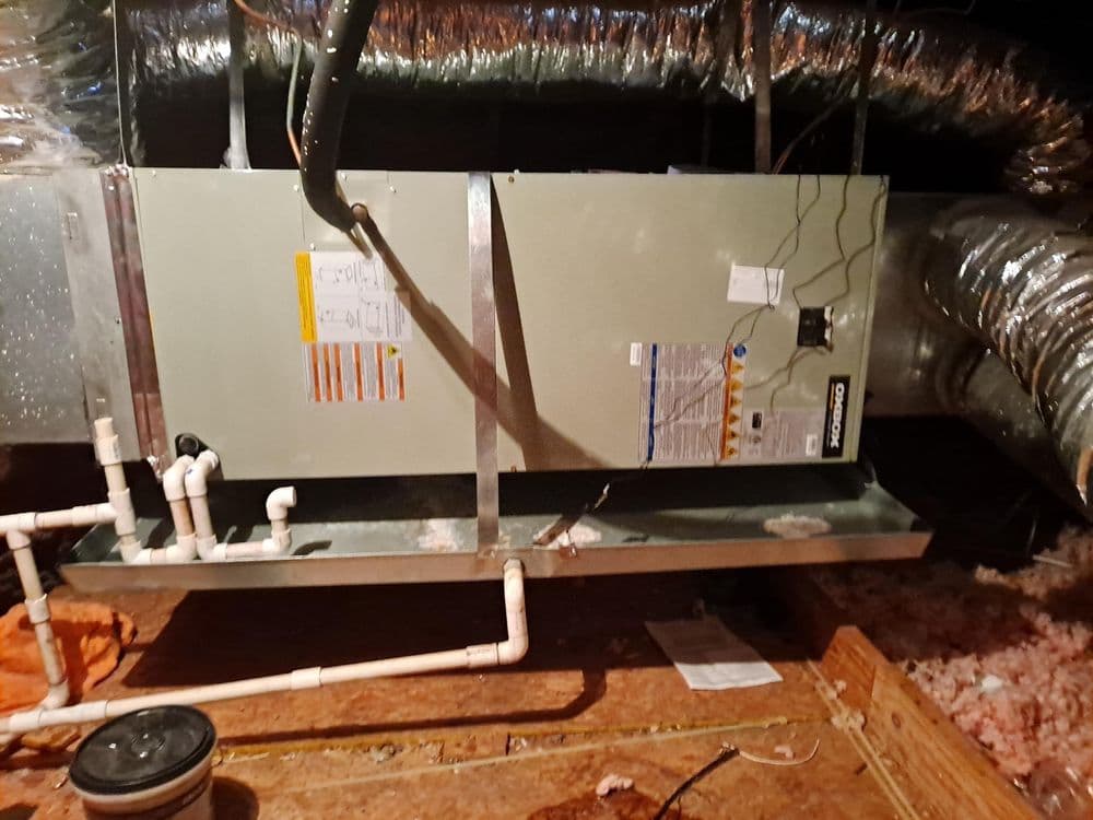 Industrial HVAC system in an attic with insulated ducts and plumbing connections.