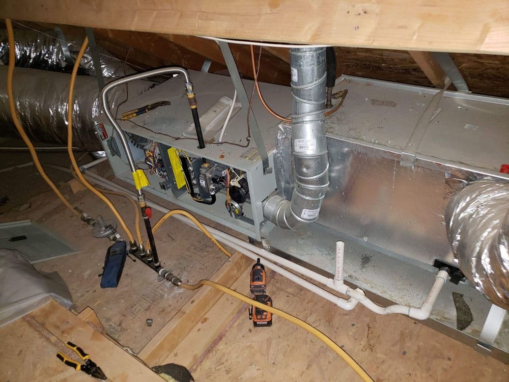 HVAC system installation in attic with ductwork and tools visible.