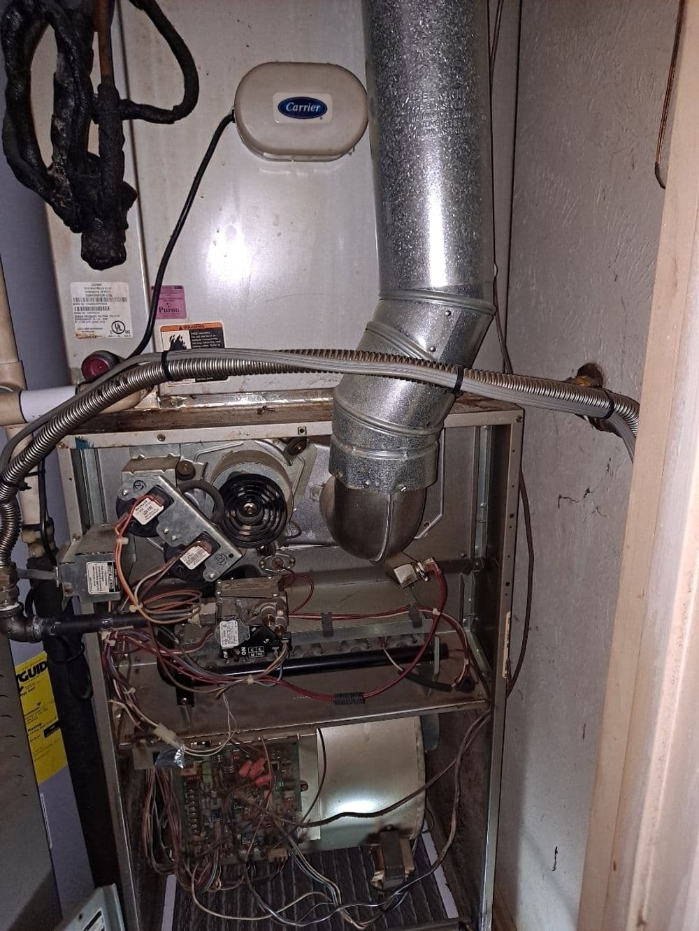 Carrier furnace showing internal components and exhaust duct in a residential setting.