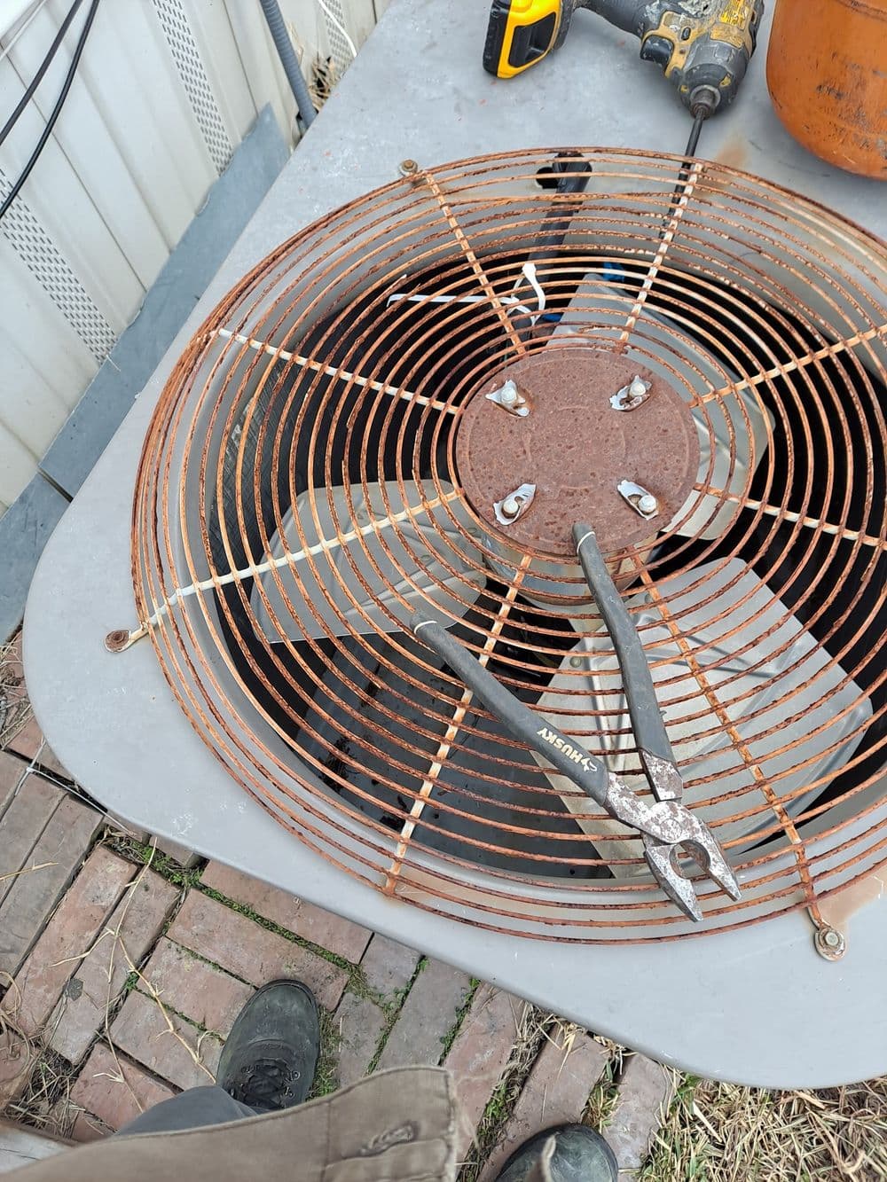 Rusty air conditioning fan with pliers on a work table outdoors.