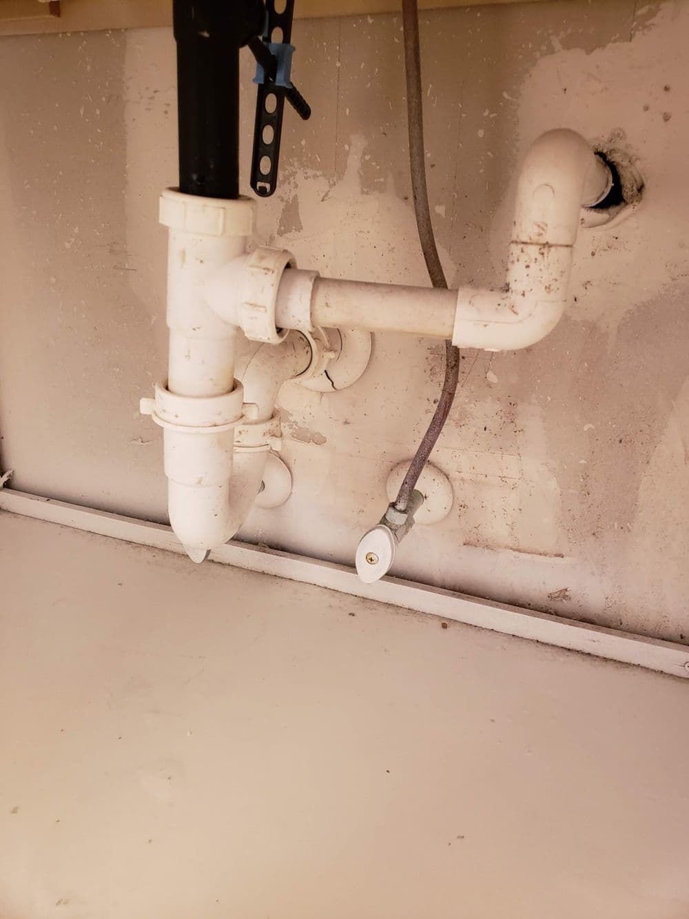 Under-sink plumbing with PVC pipes and a drain trap in a kitchen setting.