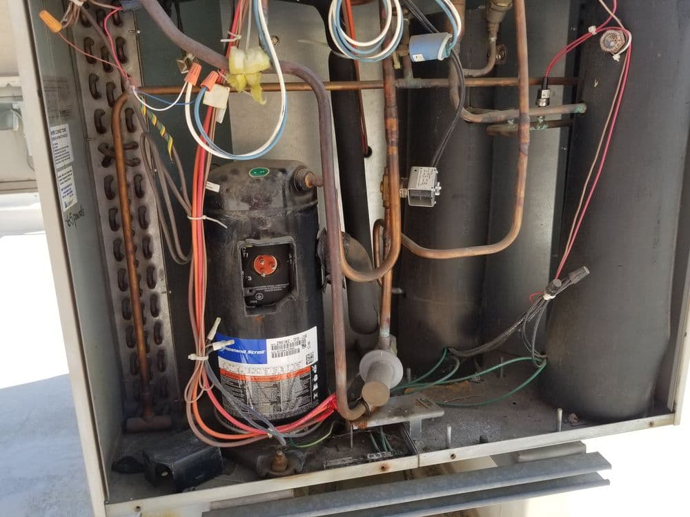 Inside view of an industrial air conditioning unit compressor with wires and tubing visible.