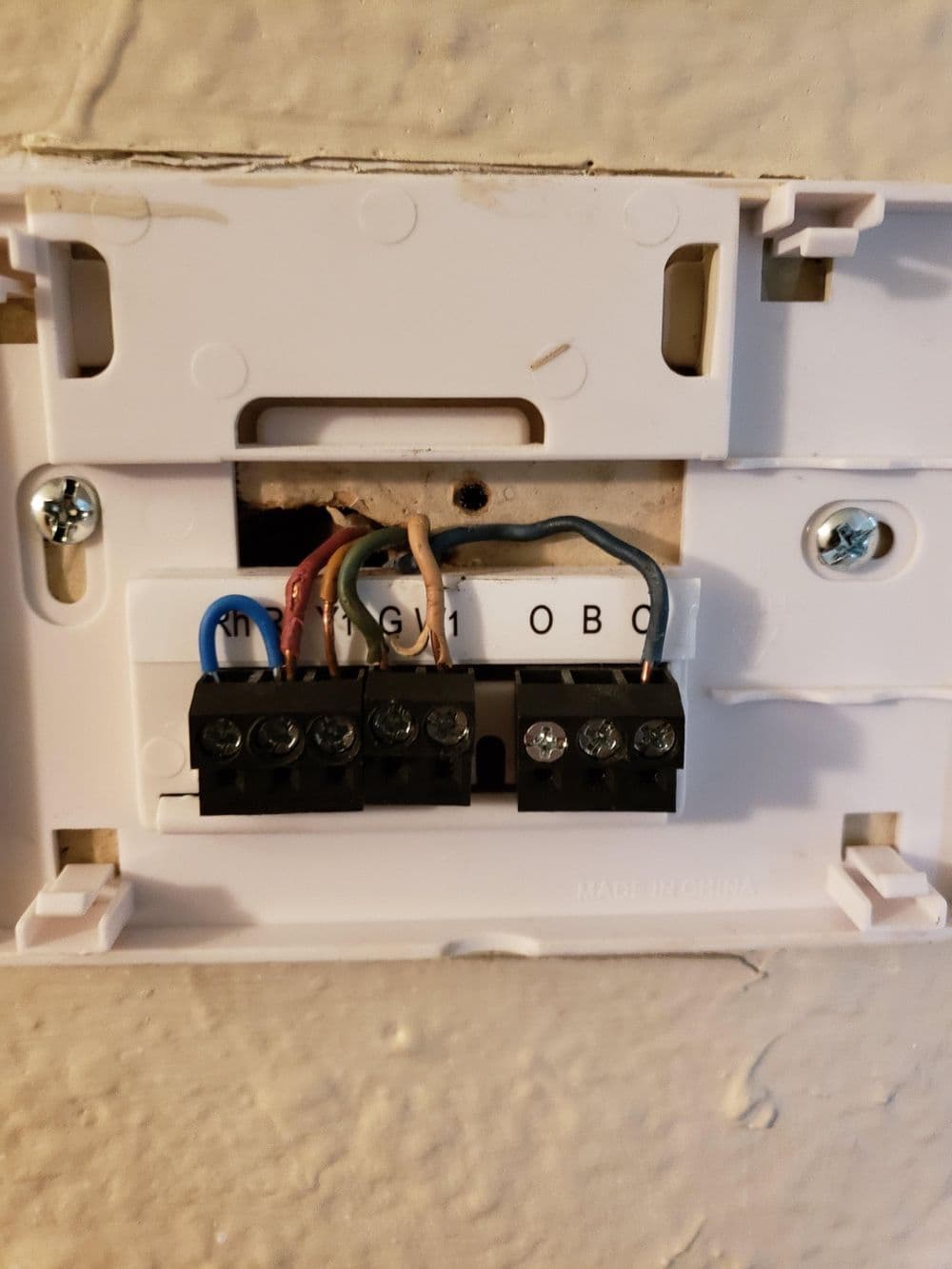 Wiring connections in a thermostat wall plate with labeled terminals and colored wires.