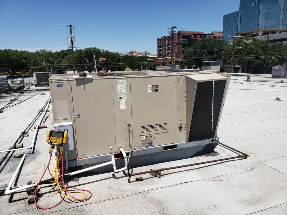 Commercial HVAC unit on a rooftop with visible pipes and hoses under a clear blue sky.
