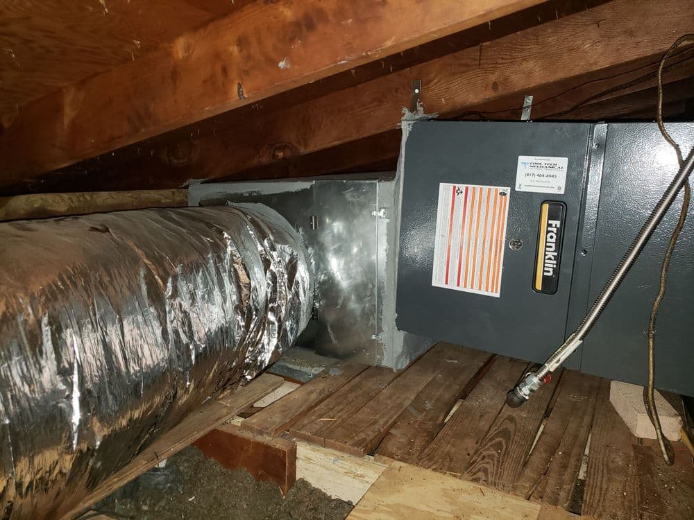 Attic heating system with ductwork and furnace, featuring shiny metal insulation.