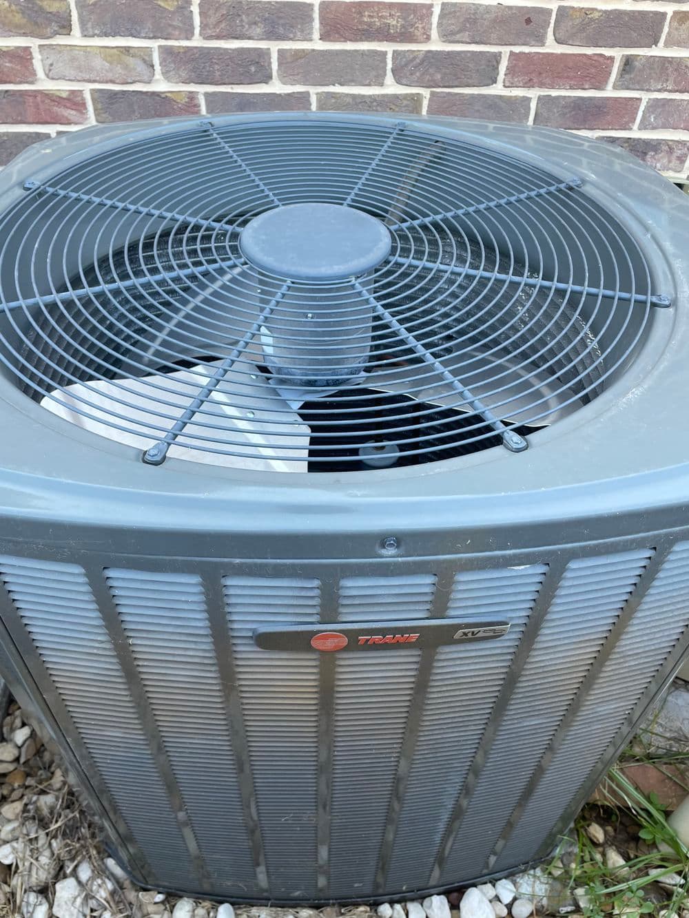 Trane air conditioning unit with fan on top, set against a brick wall.
