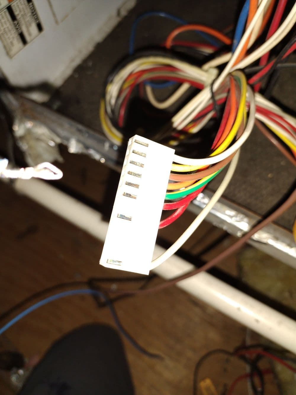 Close-up of a white connector with multiple colored wires, part of electrical wiring setup.