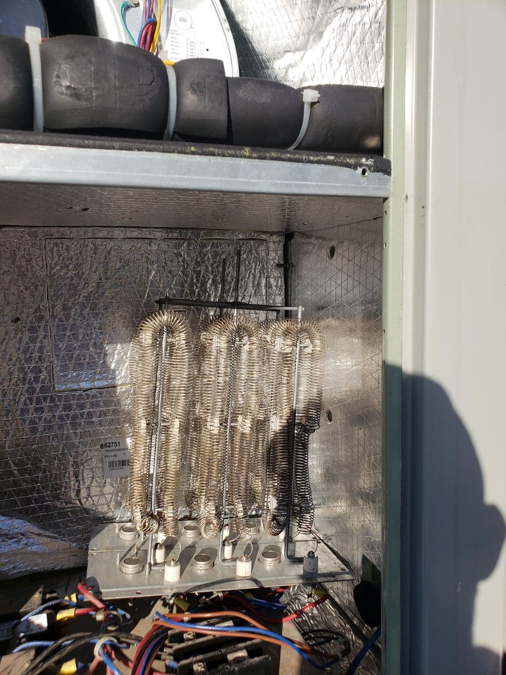 Close-up of heating coils inside an HVAC unit, showcasing wiring and metal components.